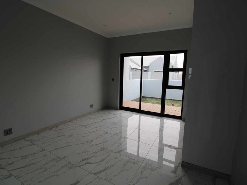 An empty living room featuring polished marble-look floor tiles and a sliding glass door providing access to a small outdoor patio area.