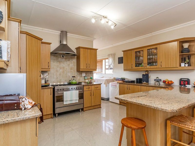 Spacious kitchen featuring granite countertops, built-in wooden cabinetry, a stainless steel gas stove with extractor fan, and a functional breakfast bar area.