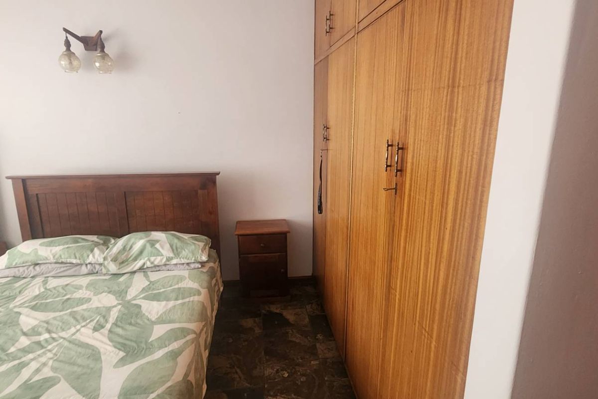 A bedroom featuring built-in wooden cupboards and a wall-mounted light fixture, offering a functional space with traditional finishes.