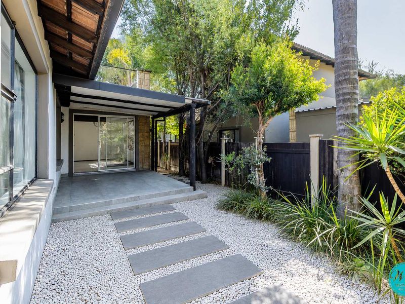 A well-maintained covered patio area featuring stone paving, leading directly into the home through sliding glass doors, set within a landscaped garden.