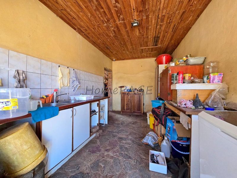 A functional scullery area featuring a sink, tiled backsplash, stone flooring, and a wooden ceiling, offering practical utility space for the home.