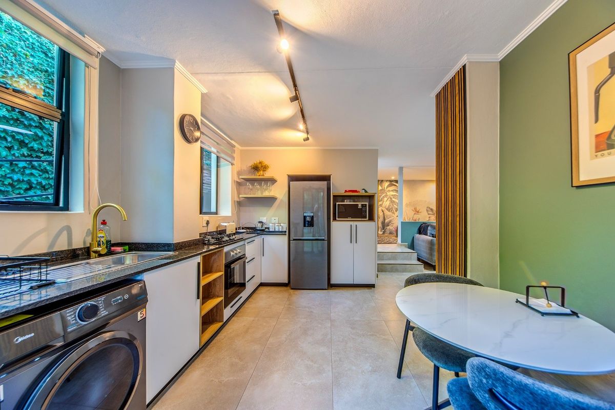 Modern kitchen featuring granite countertops, built-in oven, hob, and sleek cabinetry, seamlessly flowing into an adjacent living area with contemporary finishes.