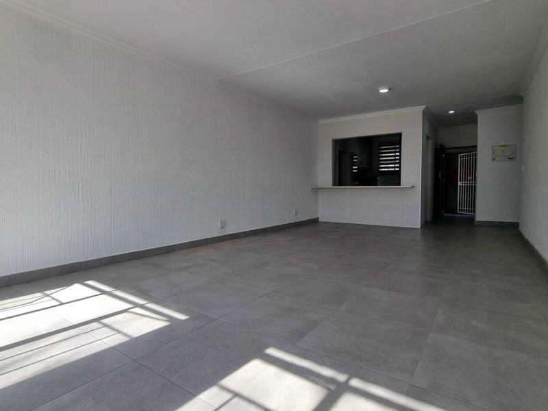 Spacious open-plan living area featuring neutral tiled flooring, textured wall finishes, and a convenient pass-through window connecting to the kitchen.