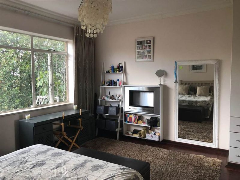 A spacious bedroom featuring large windows with security bars, hardwood flooring, and built-in wardrobe storage, offering a comfortable and functional living space.
