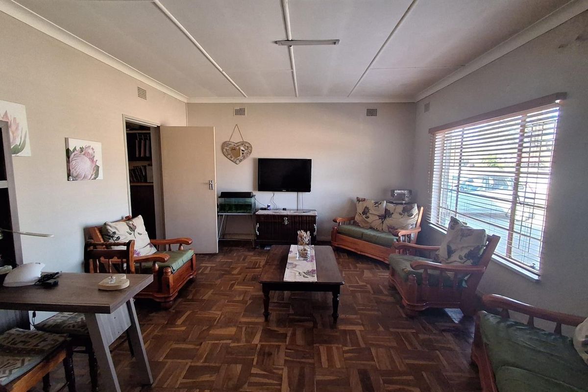 A spacious living room featuring classic parquet flooring, large windows with venetian blinds, and a neutral wall palette.