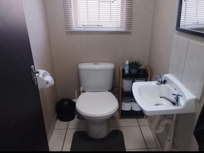 A compact guest bathroom featuring a standard toilet, wall-mounted basin, and tiled flooring with a window for natural light.