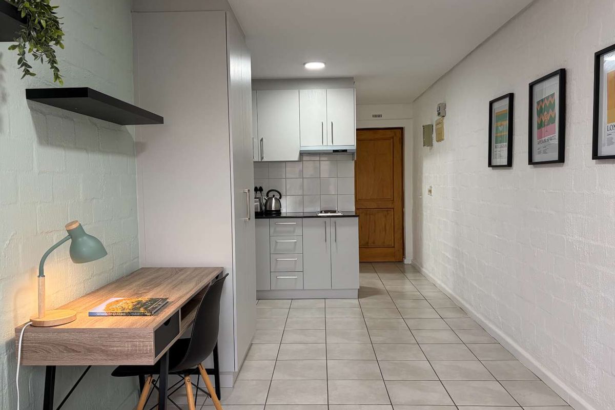 A compact kitchen area featuring modern light grey cabinetry, tiled backsplash, and neutral floor tiles, seamlessly integrated into the apartment layout.