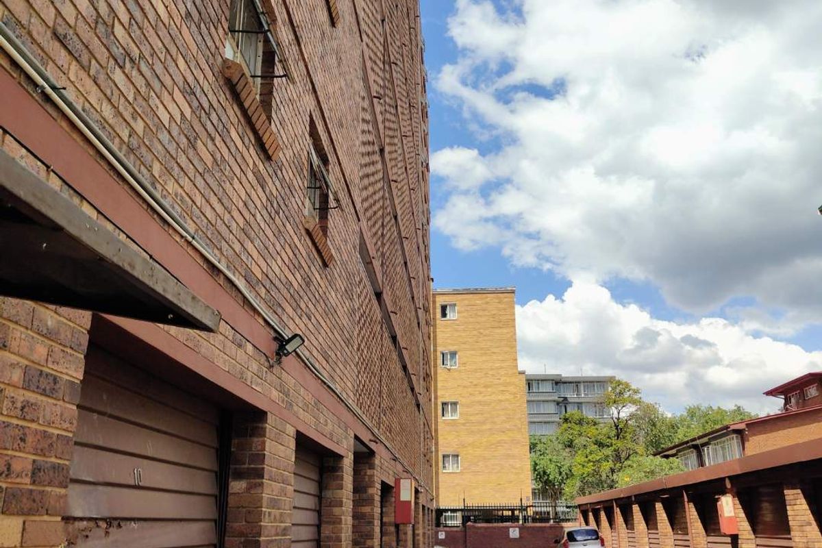Exterior view of an apartment complex showing brick facade, multiple garage units, and a paved driveway area.