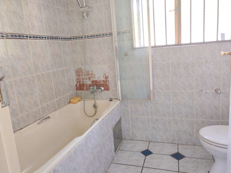 A dated bathroom featuring a bathtub with shower mixer, toilet, and tiled finishes, currently requiring maintenance and cosmetic updates to the wall tiling.