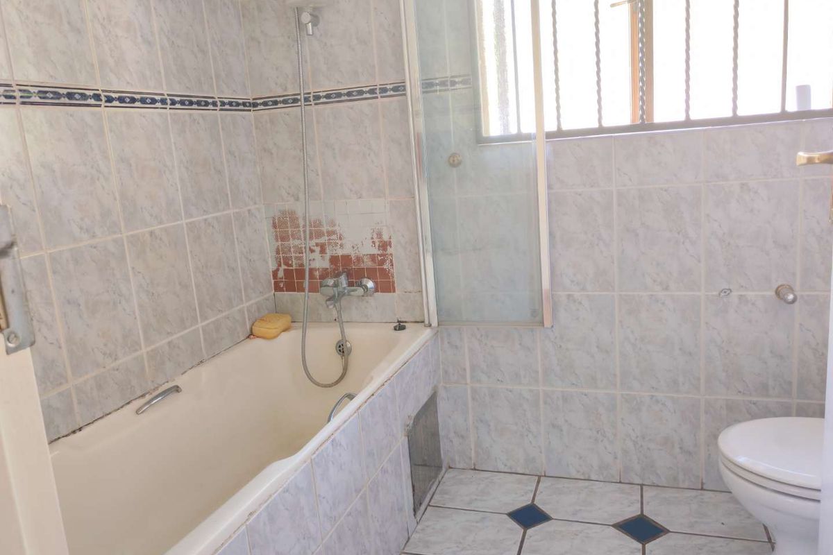 A dated bathroom featuring a bathtub with shower mixer, toilet, and tiled finishes, currently requiring maintenance and cosmetic updates to the wall tiling.