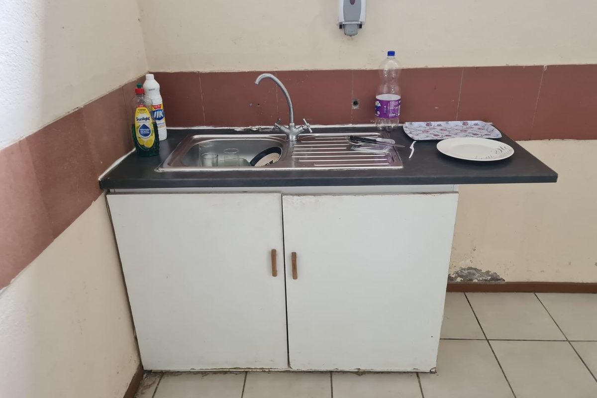 A basic kitchenette area featuring a stainless steel sink, base cabinetry, and tiled splashback, suitable for a small office or utility space.