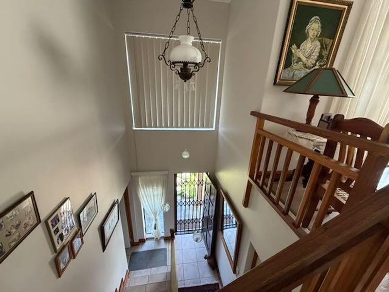 A double-volume entrance foyer featuring tiled flooring, a timber staircase railing, and a security gate, providing a bright and welcoming transition into the home.