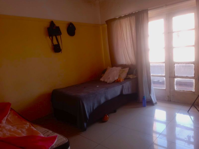 A bedroom featuring tiled flooring and access to a balcony through glass-paned french doors, requiring cosmetic updates to the wall finishes.
