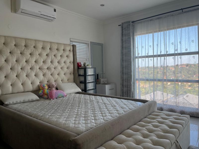 A well-maintained bedroom featuring a split-system air conditioner, recessed lighting, and a large window offering an elevated view.