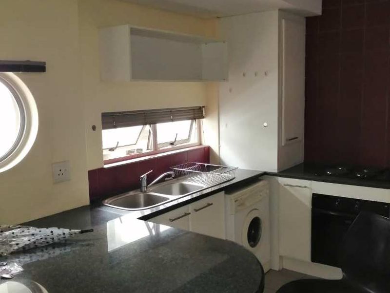A functional kitchen featuring granite countertops, built-in oven and hob, integrated washing machine, and ample cabinetry with a breakfast nook area.