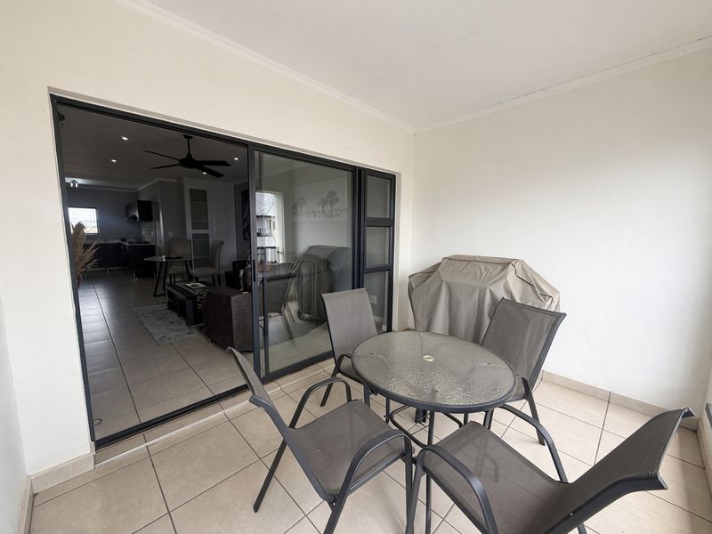 A covered balcony featuring tiled flooring and large sliding glass doors that provide seamless access to the open-plan living and kitchen area.