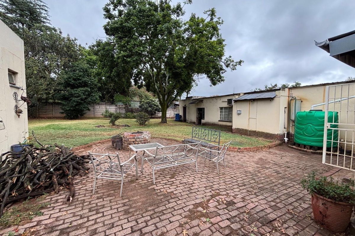 Rear exterior view featuring a brick paved patio area, built-in brick fire pit, and a water storage tank set within a garden space.