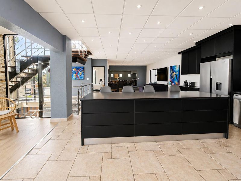 Modern open-plan kitchen featuring a large central island, sleek black cabinetry, and tiled flooring, seamlessly connecting to the living area and staircase.