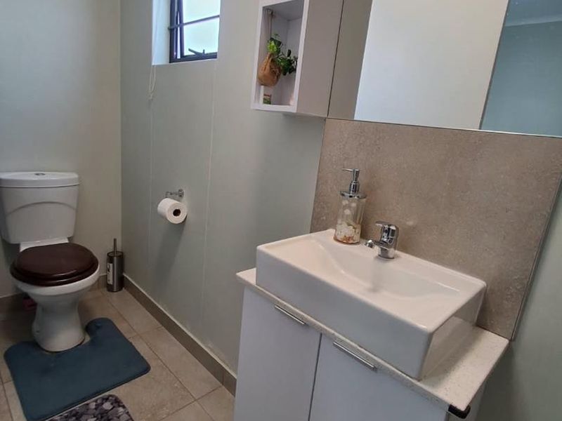 A functional bathroom featuring a modern vanity with basin, wall-mounted storage, toilet, and tiled flooring with a window for natural light.