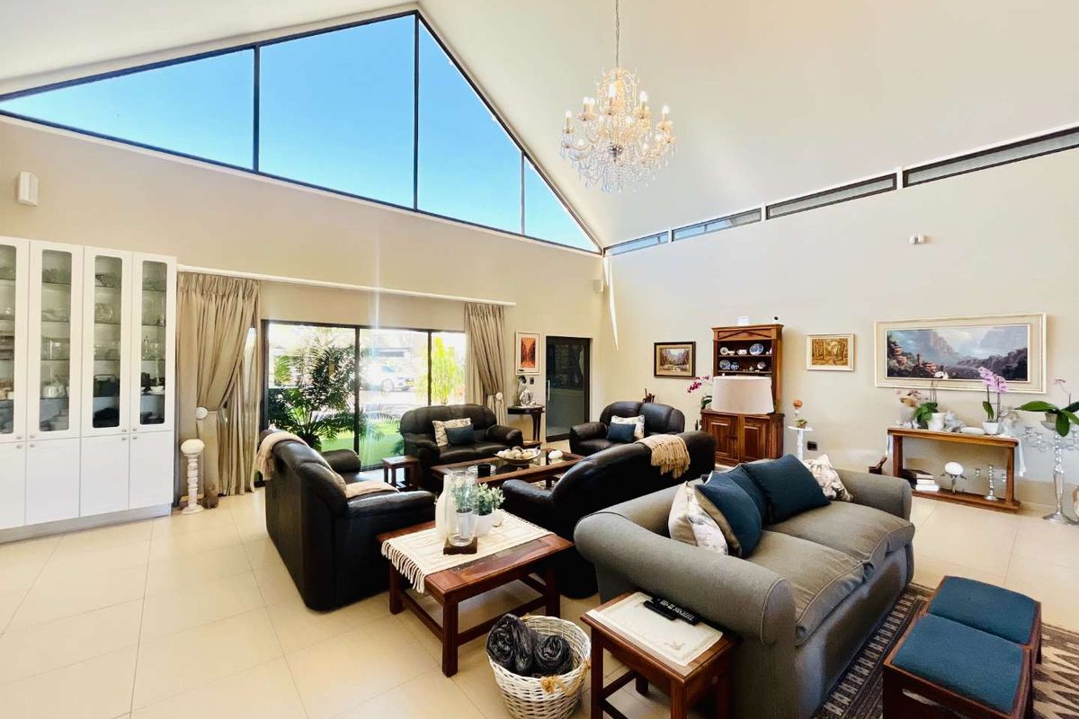 Spacious living room featuring high vaulted ceilings, large triangular feature windows, tiled flooring, and a classic chandelier, creating a bright and airy atmosphere.