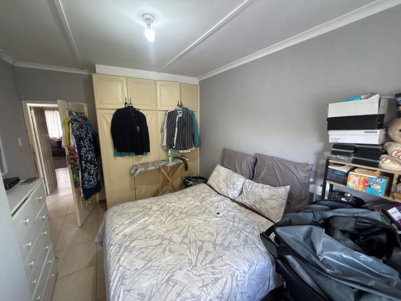 A bedroom featuring built-in cupboards, tiled flooring, and coved ceiling details, offering a functional space with potential for modernization.