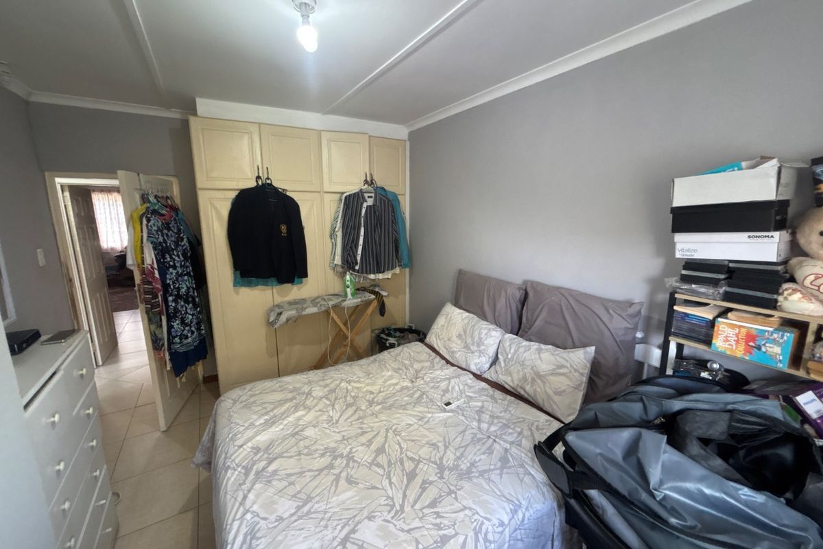A bedroom featuring built-in cupboards, tiled flooring, and coved ceiling details, offering a functional space with potential for modernization.