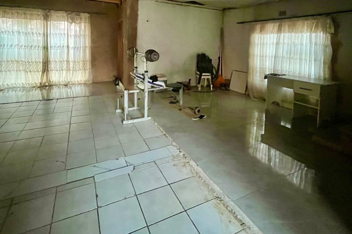 Spacious living area featuring tiled flooring and sliding glass doors, currently requiring significant cosmetic updates and floor repairs.