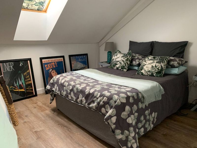 A cozy attic bedroom featuring a sloped ceiling, a skylight window for natural light, and modern laminate flooring.