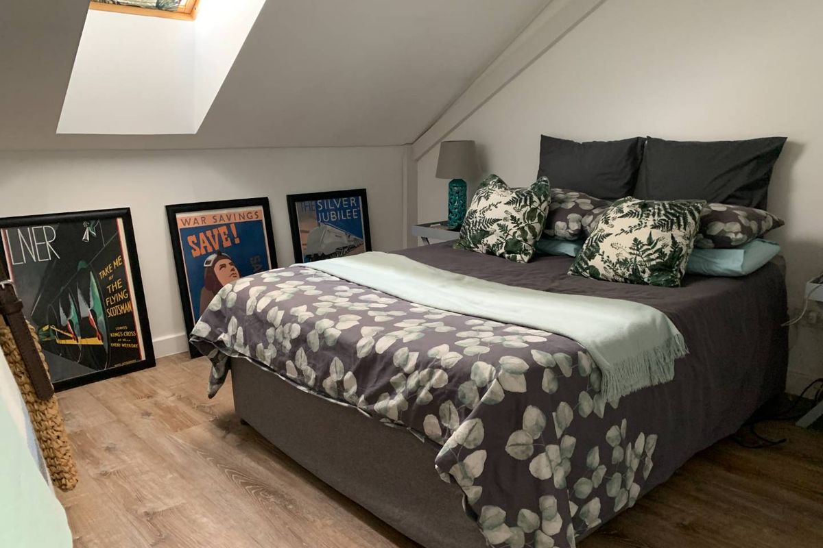A cozy attic bedroom featuring a sloped ceiling, a skylight window for natural light, and modern laminate flooring.