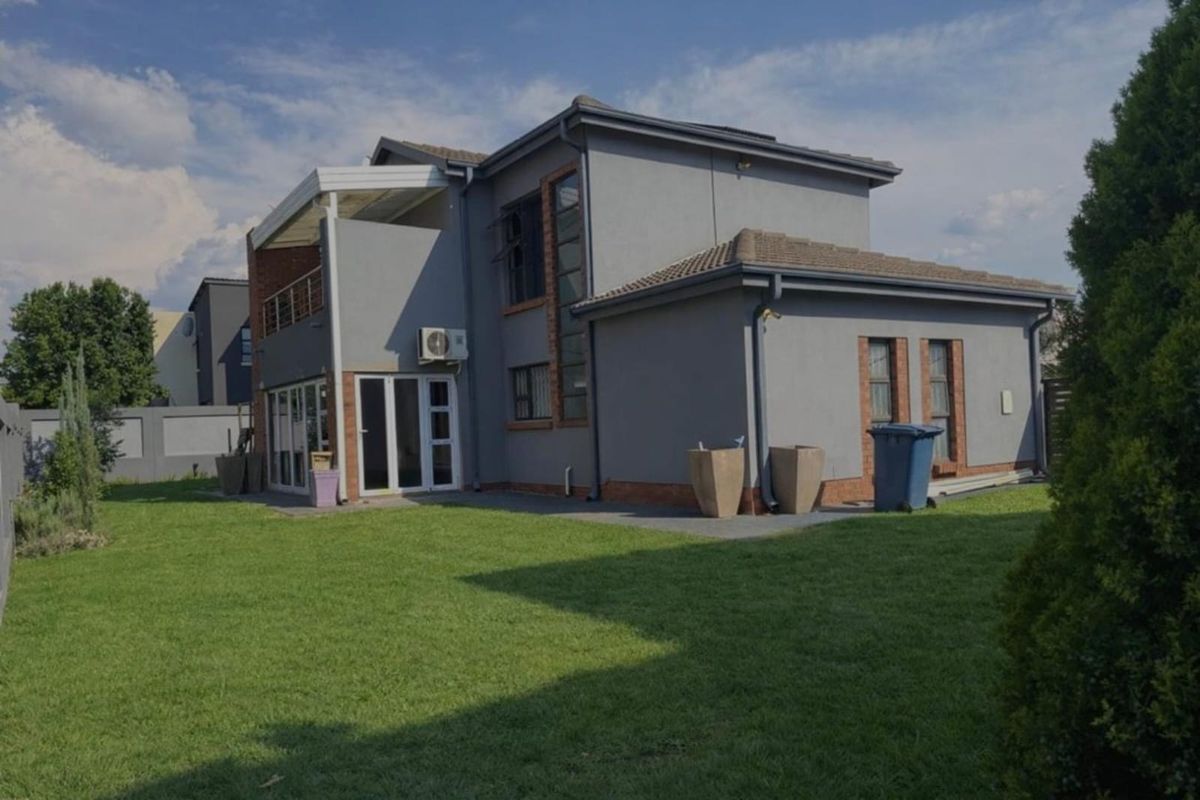 Rear view of a two-story residential house featuring a lawn, balcony, and modern plastered brick exterior finishes.