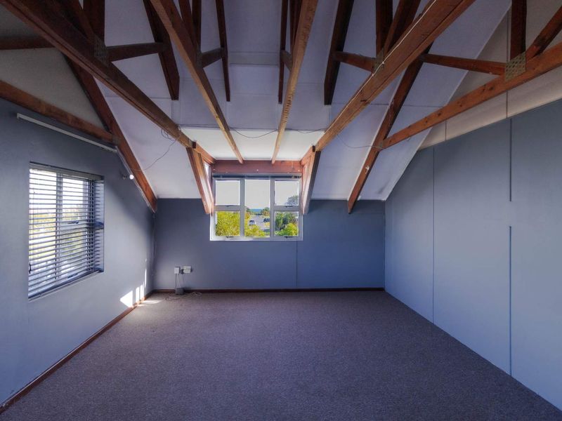 Spacious attic-style bedroom featuring exposed timber roof trusses, carpeted flooring, and large windows providing natural light and views.