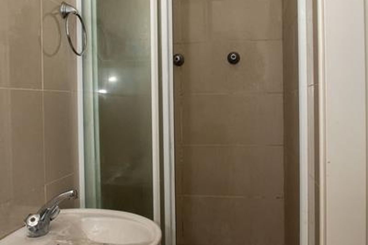 A compact bathroom featuring a pedestal basin and a corner shower enclosure with tiled walls and flooring.