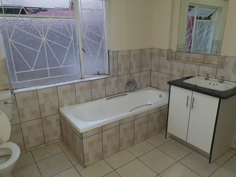 A functional bathroom featuring a built-in bathtub, vanity cabinet with basin, and tiled finishes. The space is clean but dated.