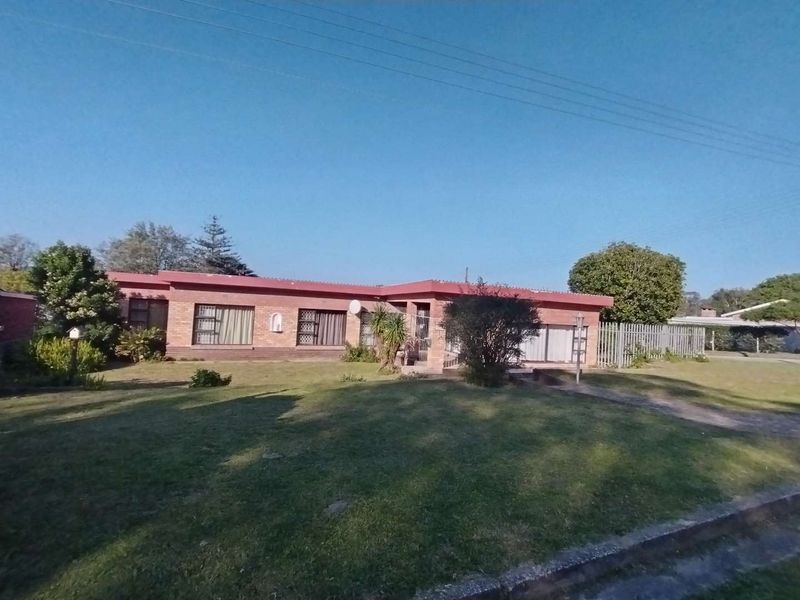 Single-story face brick family home featuring a large front lawn, metal security gates, and established garden surroundings.