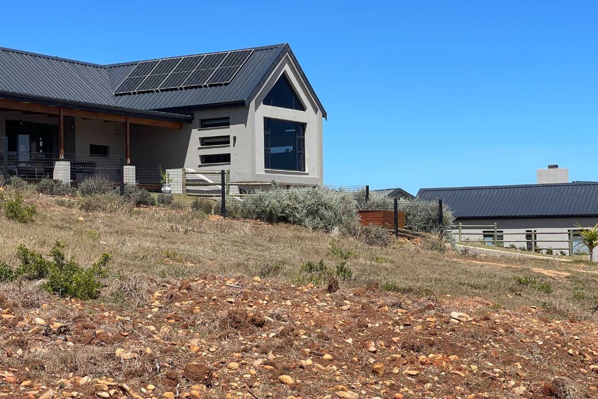 View of a modern residential property featuring a pitched roof, solar panels, and landscaped surroundings on a sloped plot.