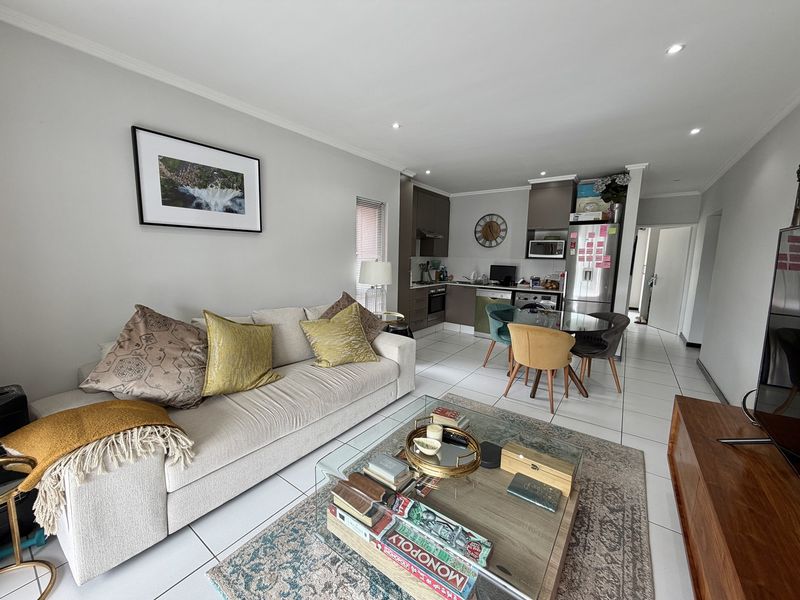 An open-plan living and kitchen area featuring tiled flooring, modern cabinetry, and integrated kitchen appliances, creating a functional and cohesive living space.