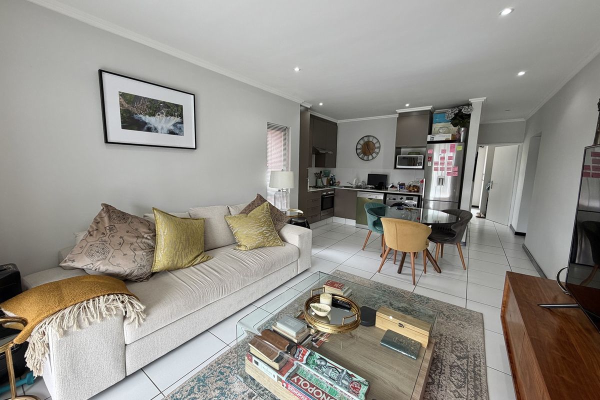 An open-plan living and kitchen area featuring tiled flooring, modern cabinetry, and integrated kitchen appliances, creating a functional and cohesive living space.