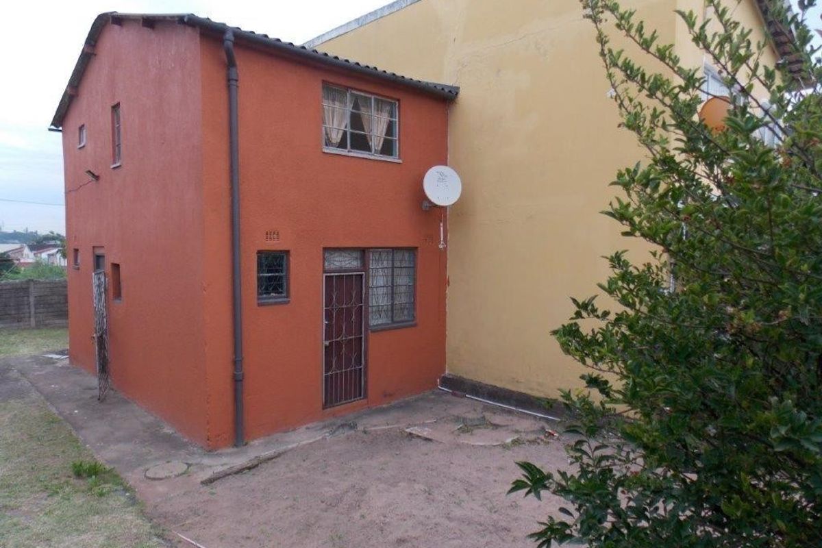 Rear view of the property showing a two-story structure with security features, satellite dish, and an adjacent concrete area with surrounding garden space.
