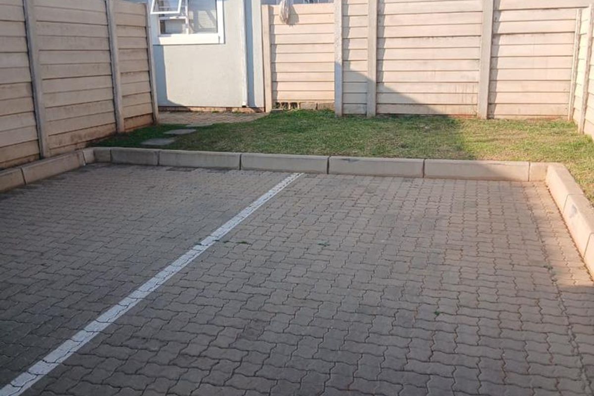 A private rear exterior area featuring a paved parking space, a small lawn, and secure precast concrete boundary walls.