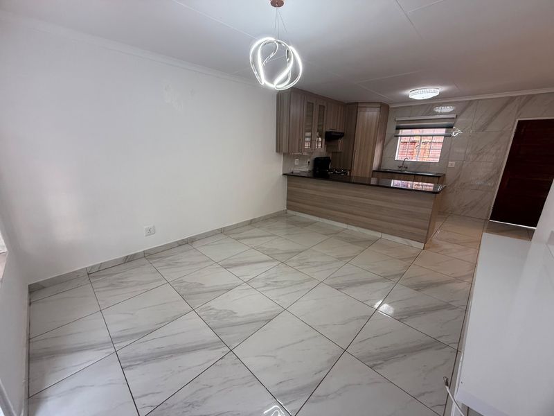Spacious open-plan living and kitchen area featuring modern marble-look floor tiles, sleek cabinetry, granite countertops, and contemporary lighting fixtures.