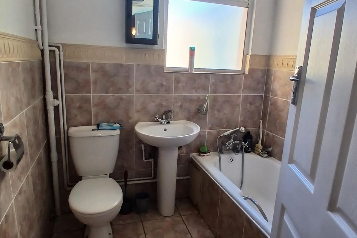 A functional bathroom featuring a pedestal basin, toilet, and bathtub with tiled finishes and exposed plumbing.