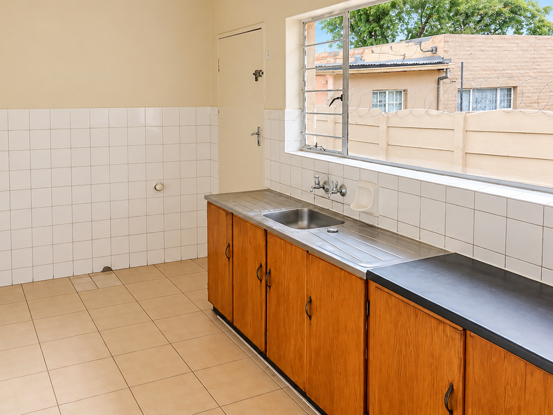 A functional, empty kitchen featuring wooden cabinetry, a stainless steel sink, tiled splashbacks, and tiled flooring, offering a blank canvas for potential renovation.