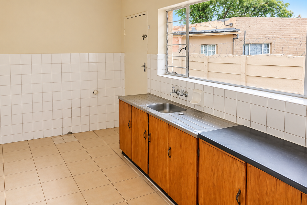 A functional, empty kitchen featuring wooden cabinetry, a stainless steel sink, tiled splashbacks, and tiled flooring, offering a blank canvas for potential renovation.