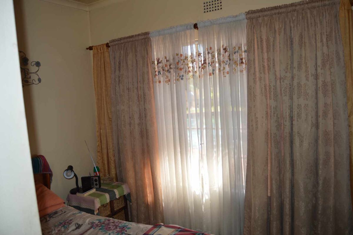 A bedroom featuring a window with layered curtains and a ventilation grille, showing standard residential finishes.