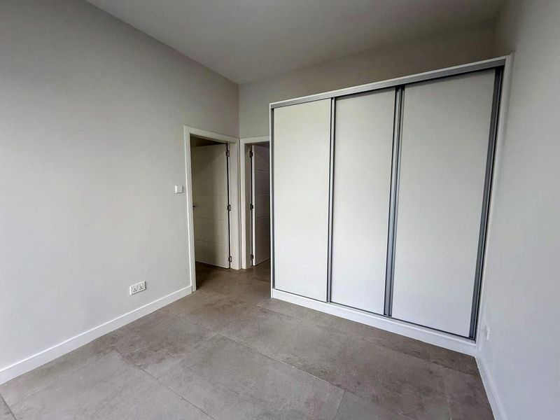 A clean, modern bedroom featuring large format floor tiles and a built-in sliding door wardrobe with a neutral finish.