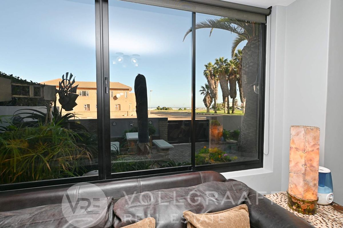 A bright living area featuring large floor-to-ceiling sliding glass doors that provide a clear view of the outdoor patio and coastal surroundings.