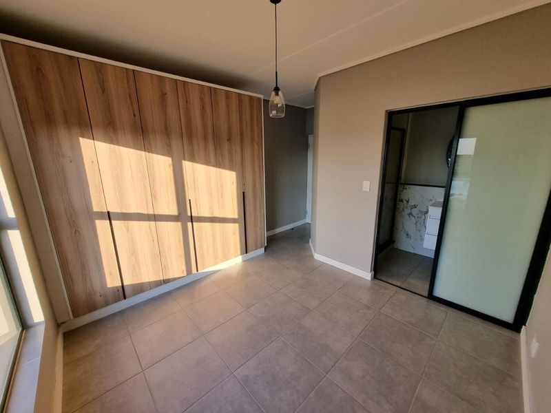 A modern, well-maintained bedroom featuring neutral tiled flooring, ample built-in wooden cupboards, and direct access to an en-suite bathroom through a sliding door.
