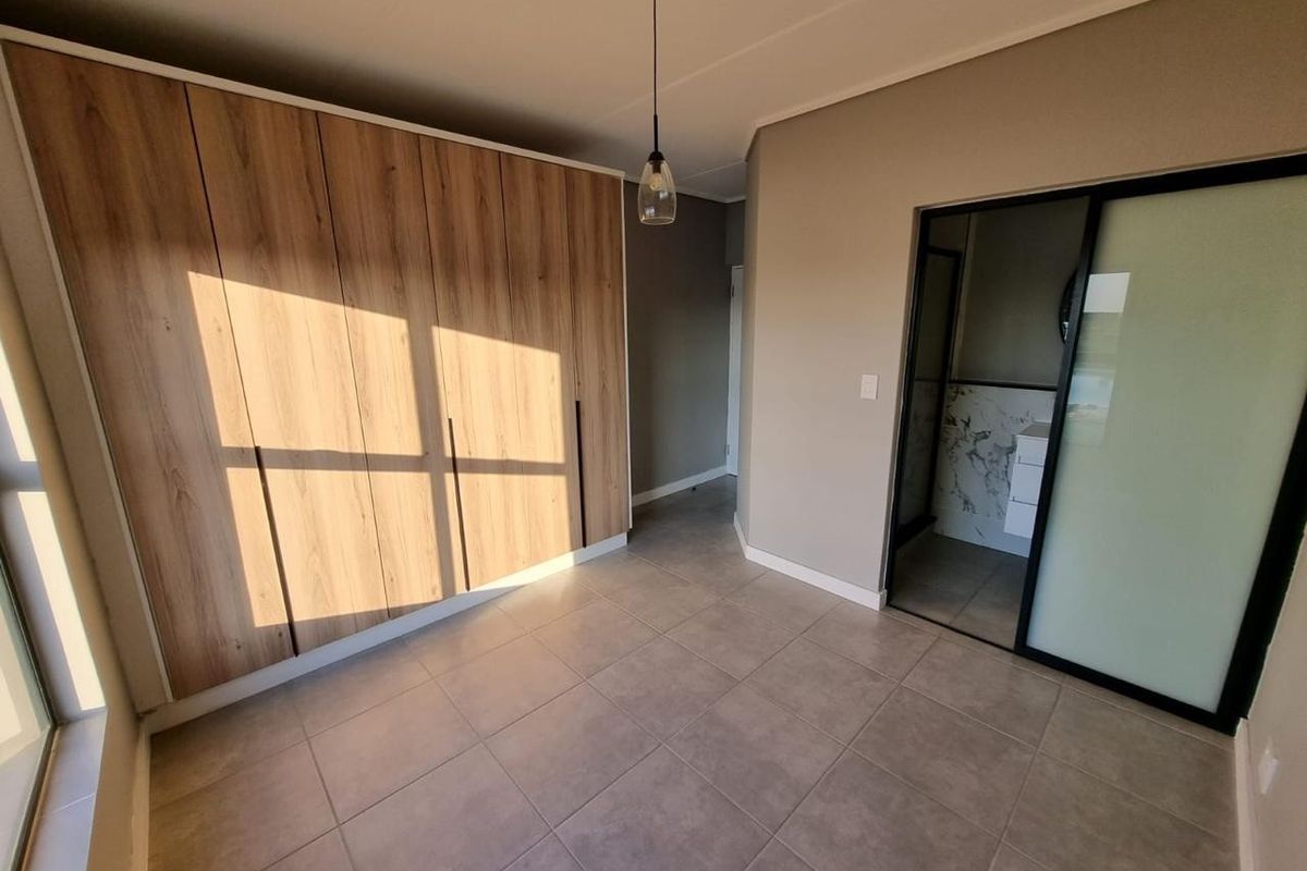 A modern, well-maintained bedroom featuring neutral tiled flooring, ample built-in wooden cupboards, and direct access to an en-suite bathroom through a sliding door.
