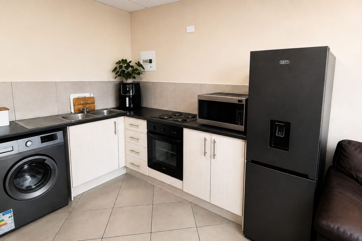 Compact kitchen featuring light-toned cabinetry, dark laminate countertops, tiled backsplash, and integrated electric oven and hob.