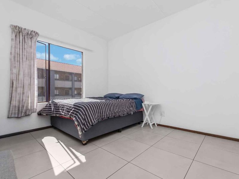 A simple bedroom featuring neutral tiled flooring and a large window providing natural light.